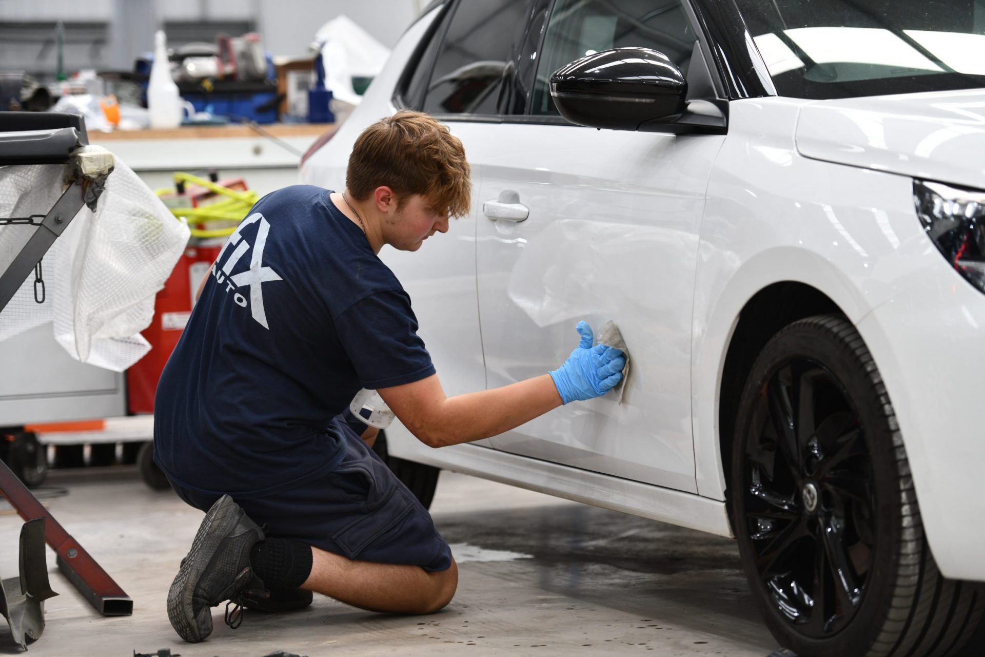 A man is repairing a white car in a workshop, focused on car body repairs in Maidensgrove.