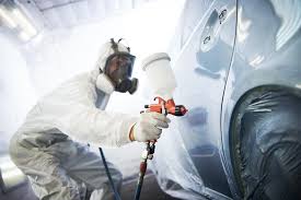 A man in a white suit sprays paint on a car, showcasing car body repairs in Slough.